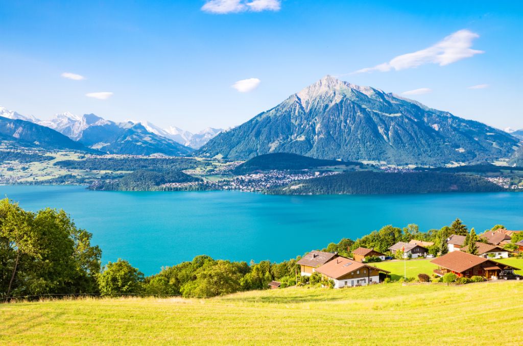 Blick von einer grünen Wiese auf einen tiefblauen See, an dessen Ufer Dörfer liegen. Im Hintergrund ragen markante, bewaldete Berge empor. Blick von einer grünen Wiese auf einen tiefblauen See, an dessen Ufer Dörfer liegen. Im Hintergrund ragen markante, bewaldete Berge empor.